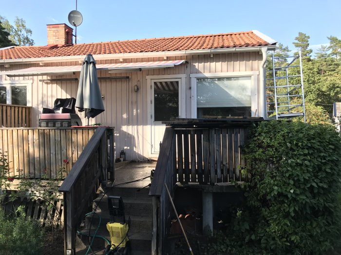 Renovering av betongaltan vid hus med brun träfasad, bortlyft trall och synligt hål vid dörrkarm.