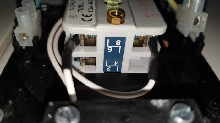 Närbild på en elektrisk anslutning inuti en apparat med märkta terminaler L, N och jordningssymbolen.