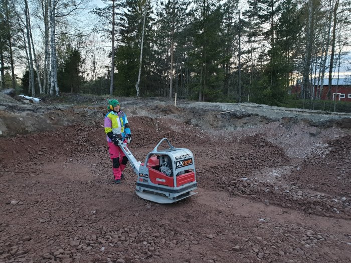 Person använder en trampplatta för att padda grus på ett byggarbetsområde.