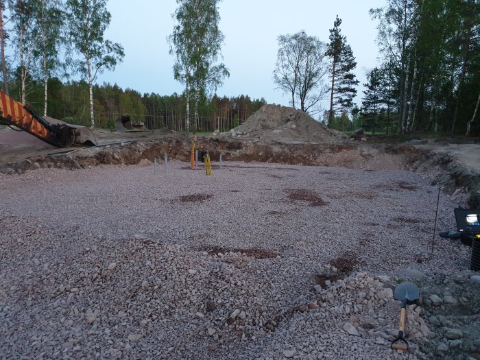 En grusad byggarbetsplats vid skymningen med utmarkerad grund och en grävmaskin i bakgrunden.