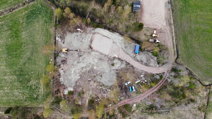 Flygbild över byggplats med grävmaskin, påbörjat garagefundament och container vid infart.