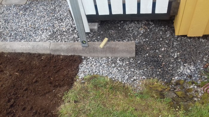 Nyplanterat gräs på jord bredvid grusgång, kantsten och del av hus med räcke.
