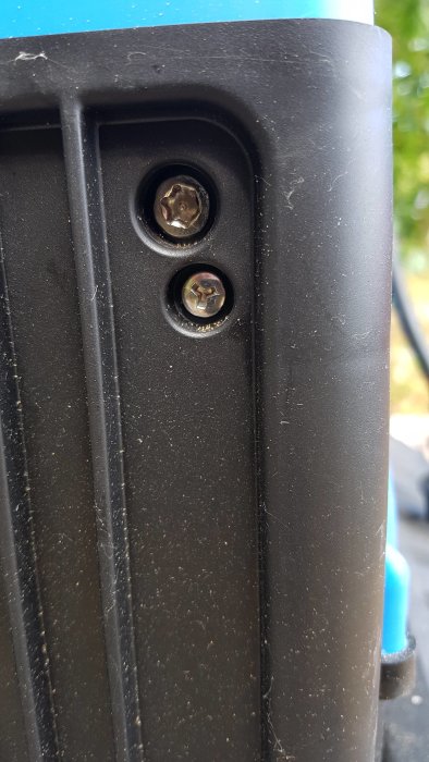 Svart plastpanel på kompostkvarn med två skruvar, en torx med pigg i mitten.