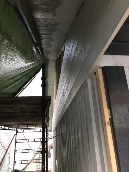Ny spikad liggande träpanel på en byggnads sida under ett taktäckt byggnadsställning.