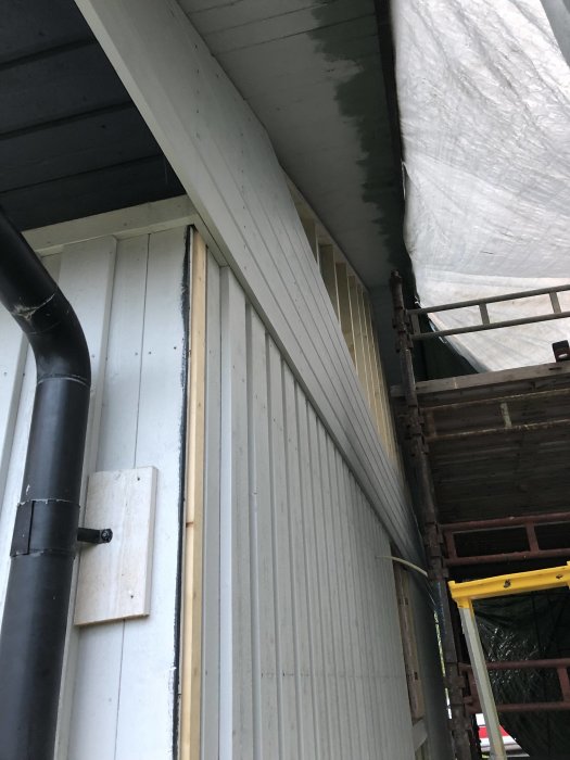 Nyinstallerad liggande träpanel på husvägg med skyddsduk och synlig ställning.