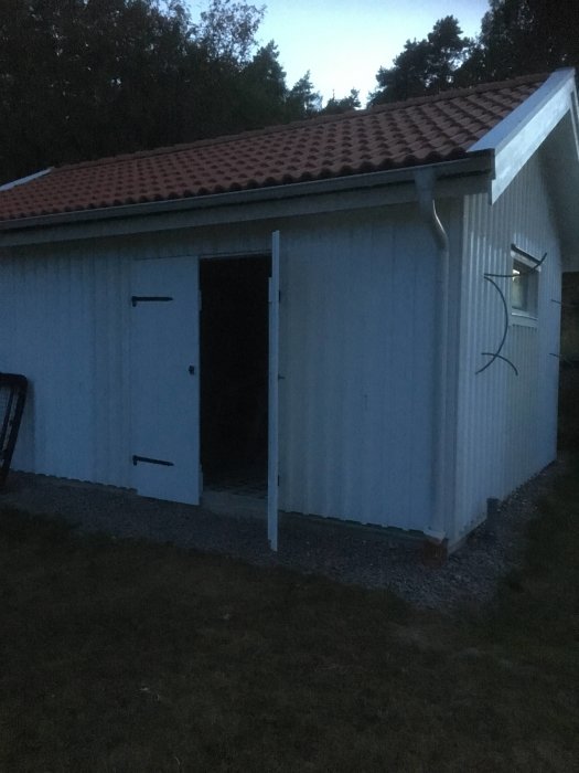 En byggnad vid skymning med isolerade ytterväggar och en öppen oisolerad dörr.