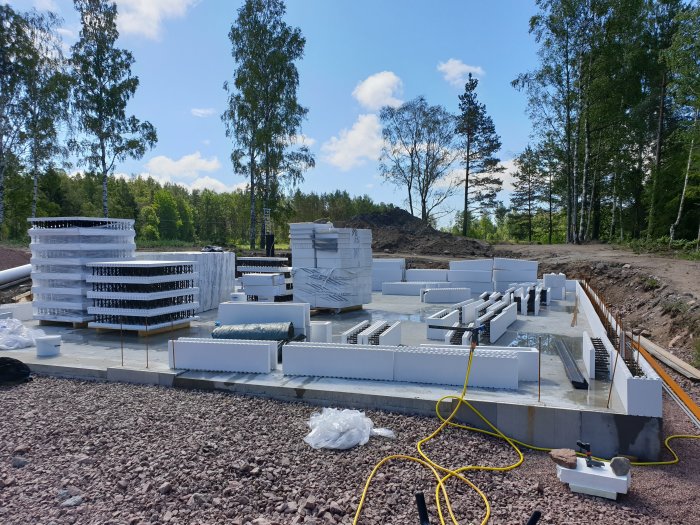 Byggmaterial för isolering och armering ligger på en nygjuten betongplatta med natur i bakgrunden.