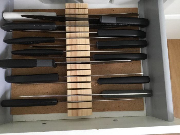 Knivar organiserade skavfötters i träblock av bonnfura och masonit i en kökslåda.