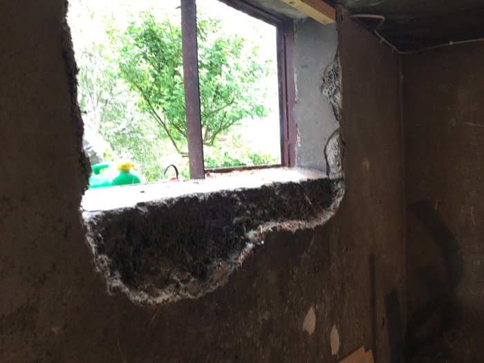 Stor skada i en betongvägg med en utsikt till trädgården och verktyg som skymtar i bakgrunden.