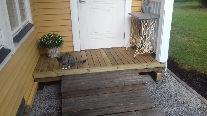 Nybyggd trätrall framför husentré med högt räcke och en katt, gula vinkelbeslag synliga.