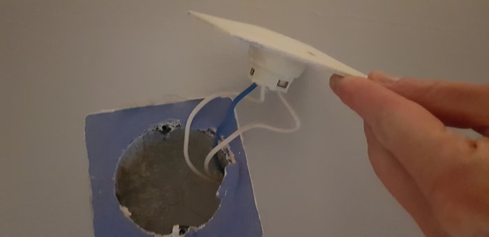 Hand håller ett ovanligt utformat takuttag med två kablar i ett blåmålat hål i taket.