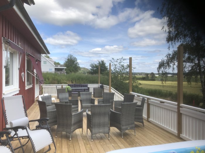 Trädäck vid rött hus med utemöbler, utsikt över öppet landskap och himmel.