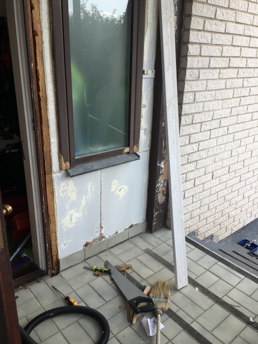 Fukt- och mögelskadad masonit vid en veranda med verktyg och renoveringsmaterial på klinkergolv.