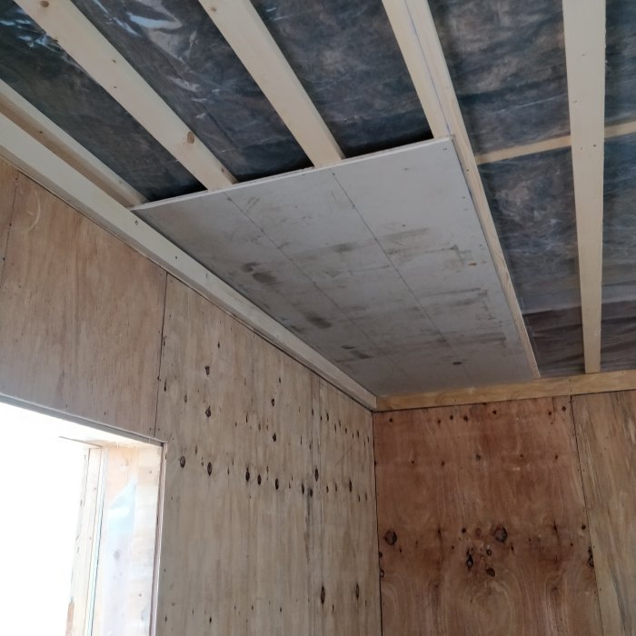 En verkstad under konstruktion med isolering, plywoodväggar och halvfärdigt gipstak.