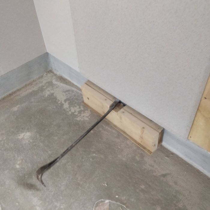Ett hörn av ett rum under renovering, med en kofot lutad mot en träblock för att lyfta en gipsskiva.