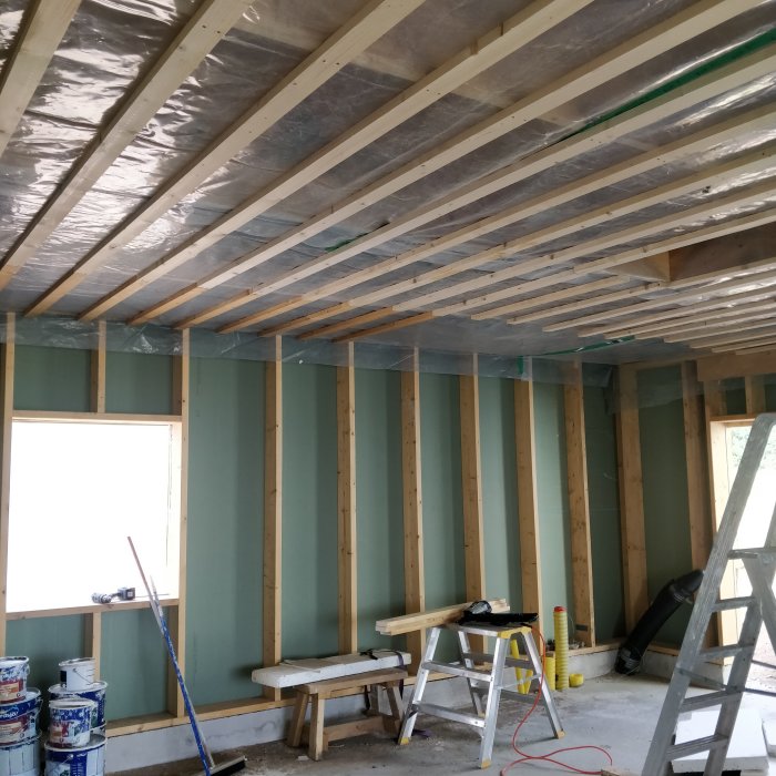 Renoverad verkstad med isolerade väggar och gips under taket, byggmaterial och verktyg syns.