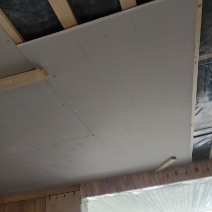 Nyinstallerade gipsskivor på verkstadens tak med synliga skruvhuvuden och träreglar.
