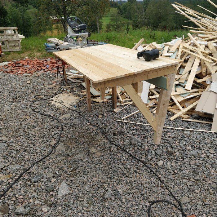 Hemsnickrat skärmtak under konstruktion utomhus med sågbänk och virke i bakgrunden.
