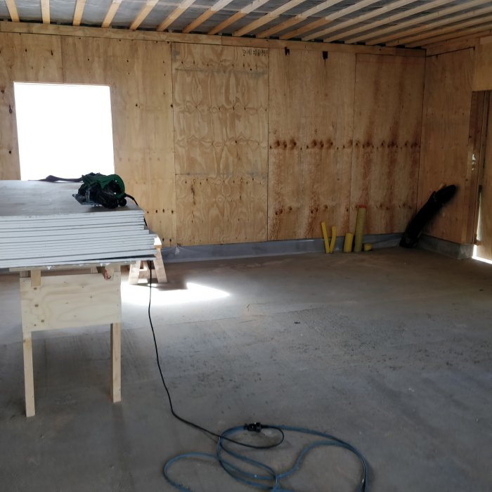 Renoverad verkstad med plywoodväggar och arbetsmaterial på sågbänk under arbetsprocess.