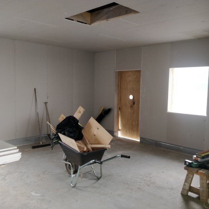 Renoverad verkstad med gipsade väggar och tak, träskivor i skottkärra, och verktyg på golvet.