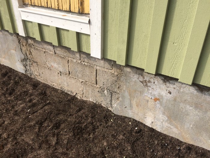 Ojämn betongvägg och tegel vid husgrund som behöver putsas.