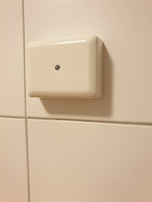 Vit plastdosa på kakelvägg som döljer en utstickande kabel.
