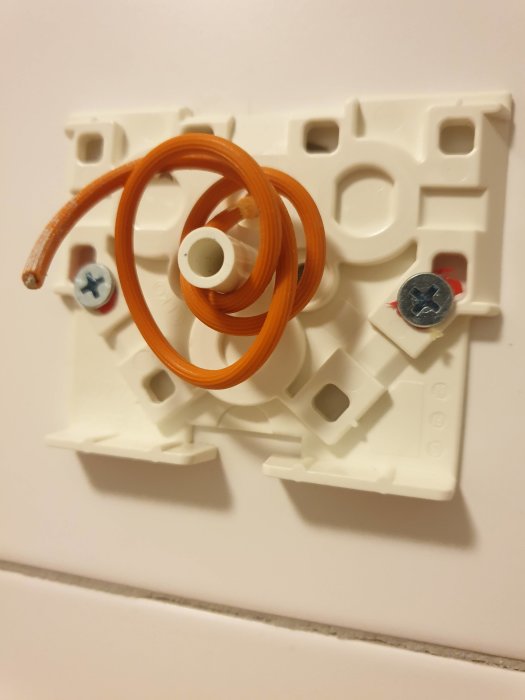 En plastdosa med en ihoprullad orange kabel och skruvar på en vägg.