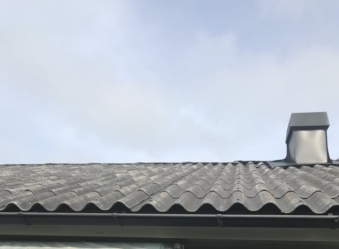 Närbild av grå nockpannor på tak med skorsten, indikerar skadade takpannor.