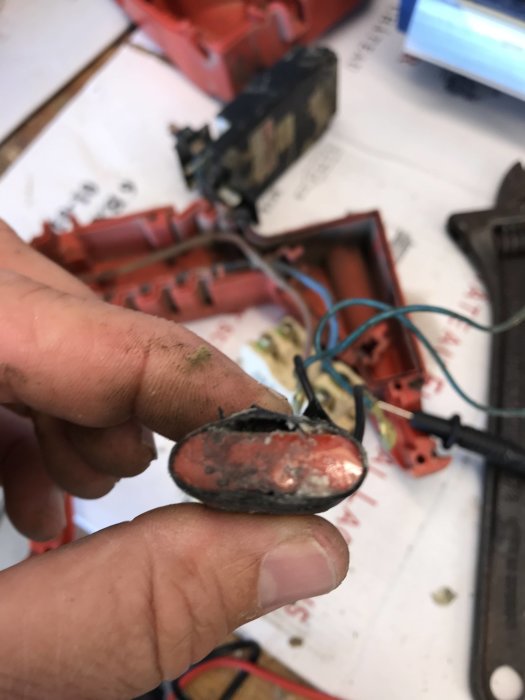 Skadad startkondensator från mejselhammare som hålls av en hand, med uppriven ände och synliga ledningar.
