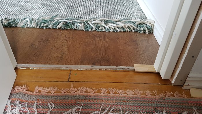 Nivåskillnad på tröskel mellan två golvtyper med öppen dörr och mattkant.