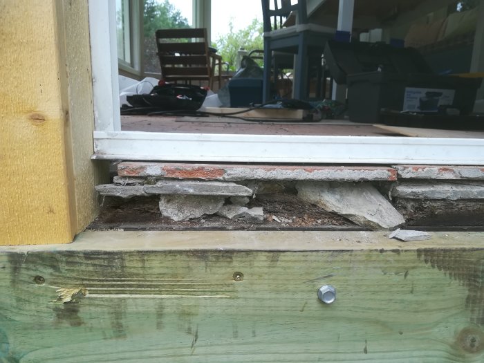 Skadad tröskel med sönderfallande mursten och betong vid en husgrund.