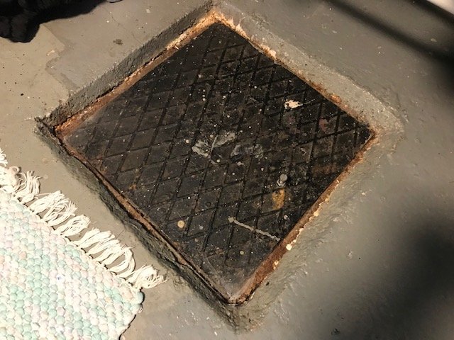 Rensbrunn med täckt betonglock av grus och sten i en källare.