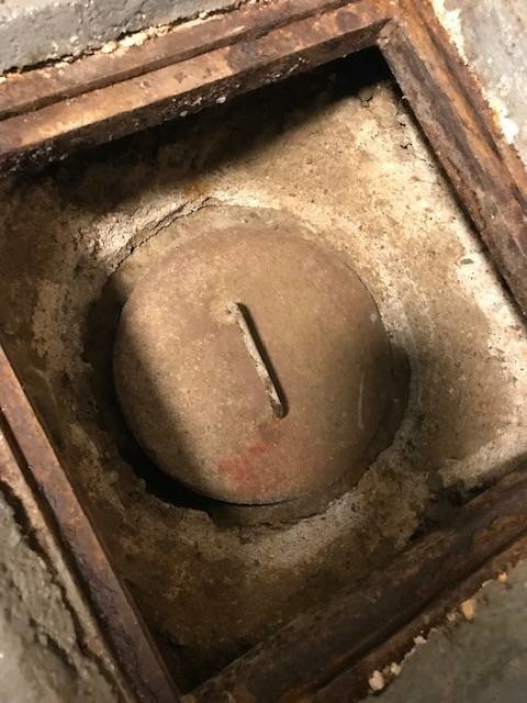 Betonglock i en rensbrunn täckt av ett lager grus och sand i en källare, med synligt glapp till röret.