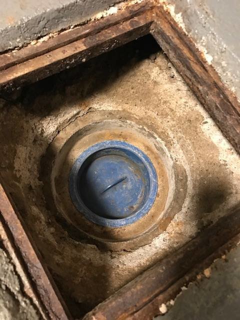 Betonglock över rensbrunn täckt av grus och sten i en villa från 1920-talet.