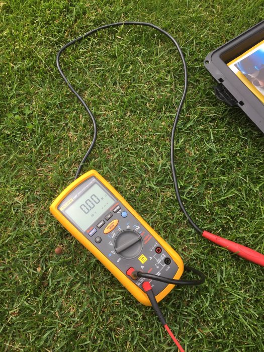 Isolationsmätare och testkablar på gräsmatta som visar 0,0M ohm under elektrisk mätning.