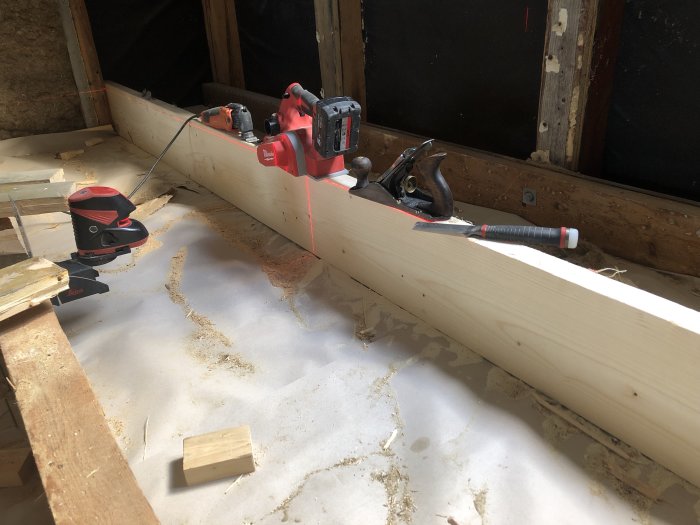 Renovering av golv med laser för att rikta nya bjälkar, med verktyg och sågspån runtomkring.