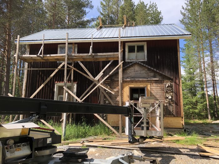 Ett hus under renovering med ställningar och en ny hängränna, omgivet av skog.