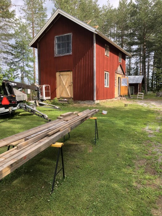 Röd träbyggnad med påbörjat takarbete bredvid lång planke på arbetsbockar, redo för montering av hängrännor.