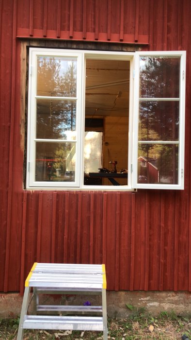 Falurödt trähus med nyinstallerat vitramat fönster och en arbetsstege framför, redo för målning och renovering.
