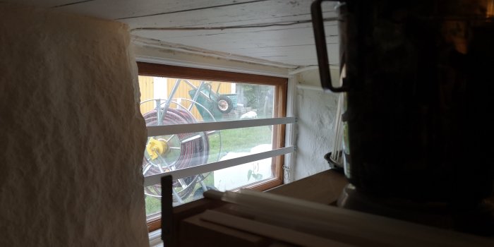 En elkabel som löper ovanför ett fönster i en källare, med utsikt mot en trädgård.