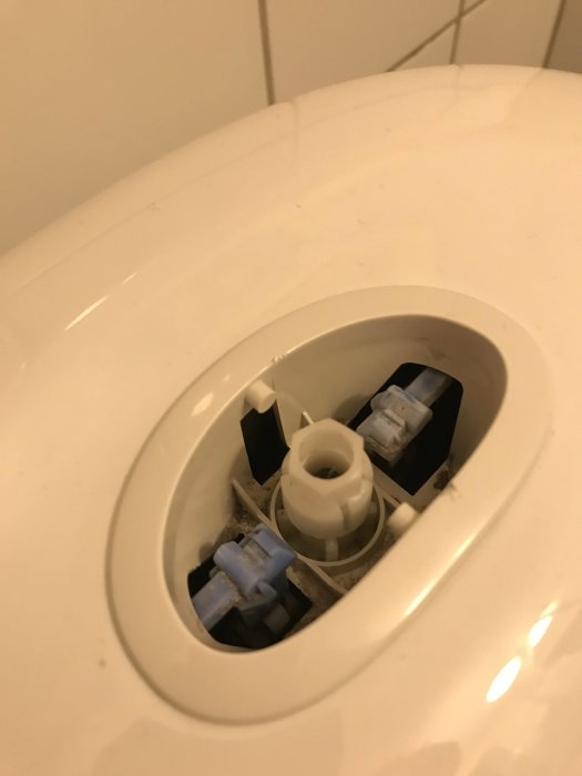 Inre mekanismen av en toalettstol med vit mutter i mitten och spolmekanismdetaljer.