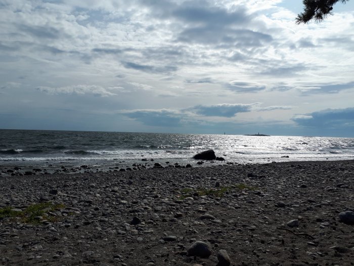 Stenig strand med vågor och moln på en blåsig eftermiddag vid havet.