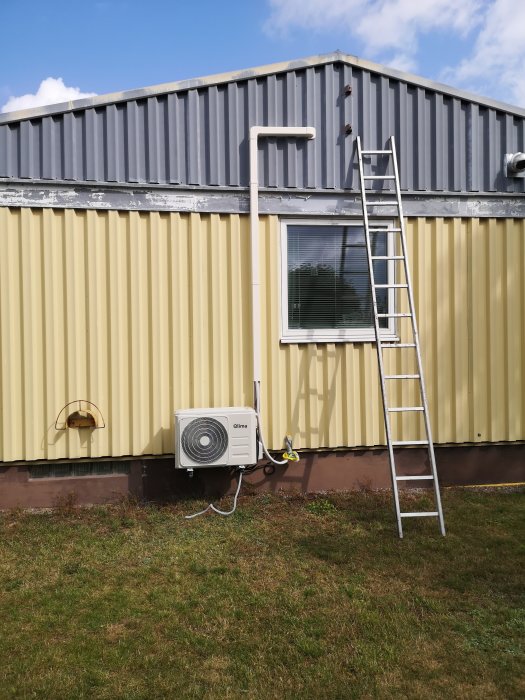 Nyinstallerad luftvärmepump vid gult hus med stege lutad mot väggen innan justering av kyltekniker.