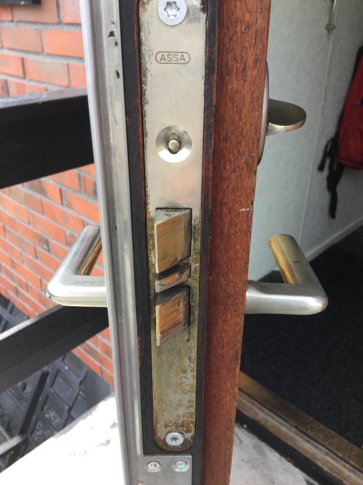 Slitet dörrlås av märket ASSA monterat på en träfärgad dörr med synlig låskista och handtag.