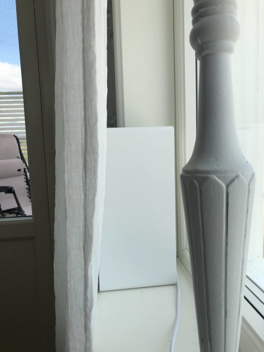IKEA/Sonos Symfonisk högtalare delvis dold bakom en vit gardin vid fönsterkanten.