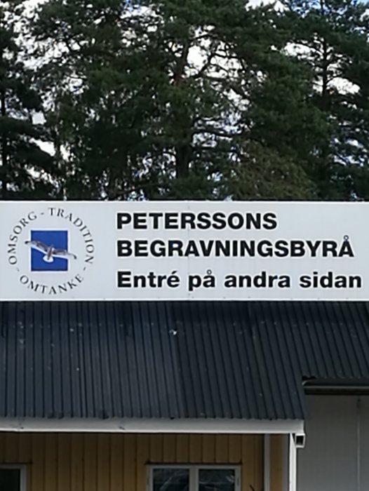 Skylt för "Peterssons Begravningsbyrå" med texten "Entré på andra sidan".