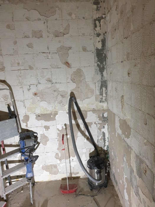 Renoverat badrum med avskrapade väggar av blandade material, dammsugare och stegar syns.