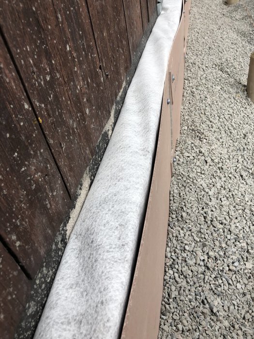 Bågnande fibercementskivor monterade mellan träaltan och grus, med synliga skruvar och tecken på förvrängning.