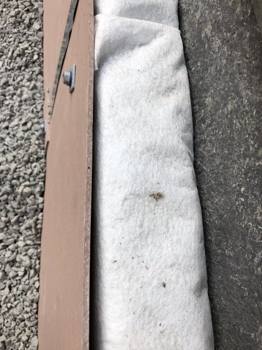 Närbild på böjda fibercementskivor monterade på en grund med synliga skruvfästen och isoleringsmaterial.