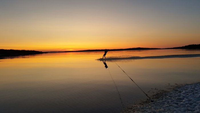 Person som wakeboardar på stilla vatten vid solnedgång.